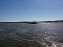 Zrcadlení se slunečních paprsků v hladině řeky Świna s nákladní lodí uprostřed.